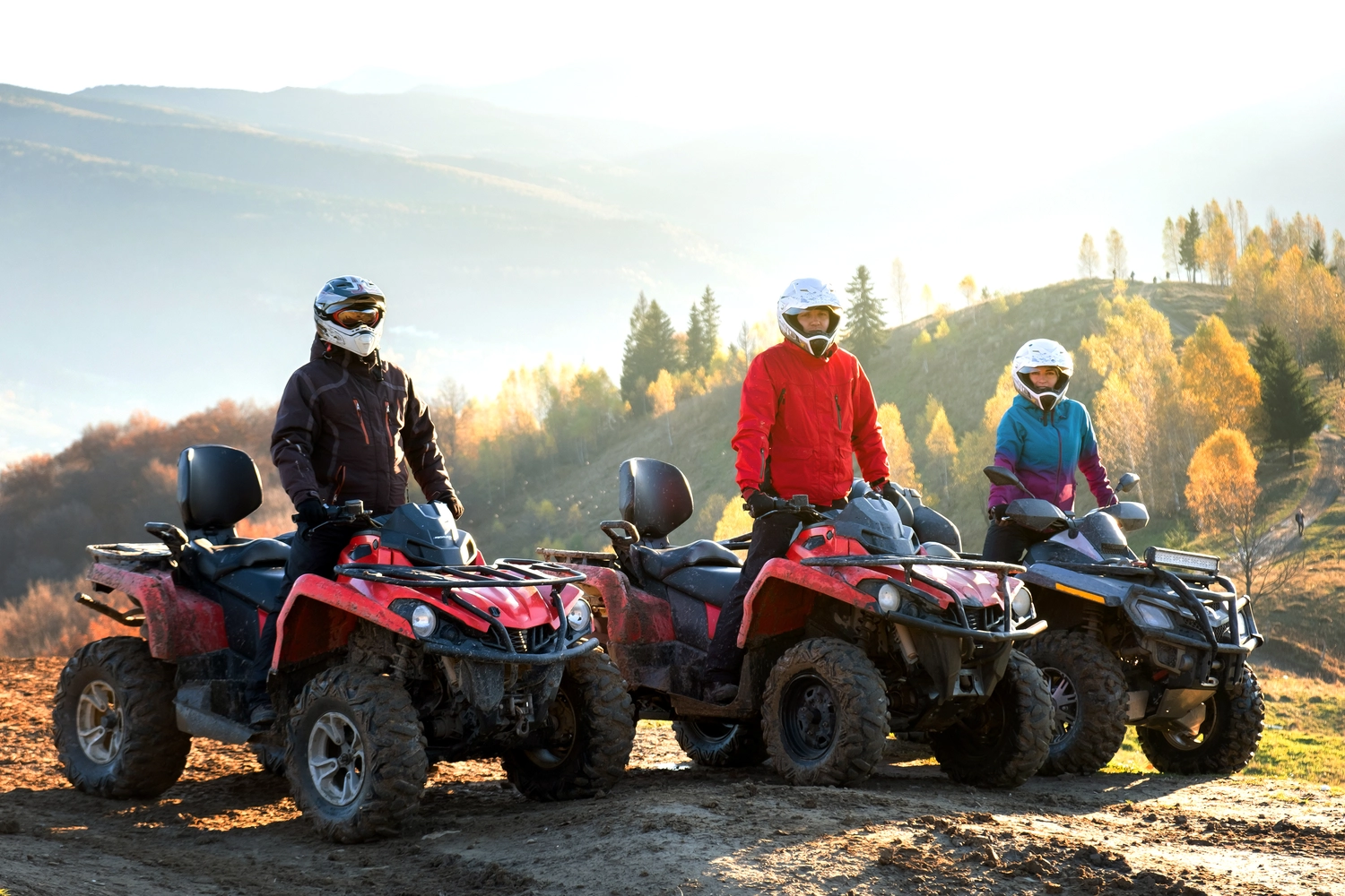 Glückliche Fahrer mit Schutzhelmen genießen bei Sonnenuntergang eine extreme Fahrt mit ATV-Quad-Motorrädern in den Sommerbergen. 